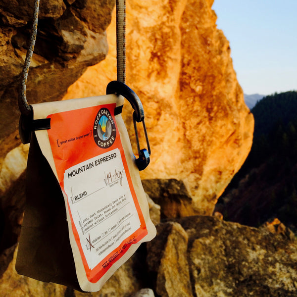mountain espresso bag hanging from sandstone cliff with pine trees in the background